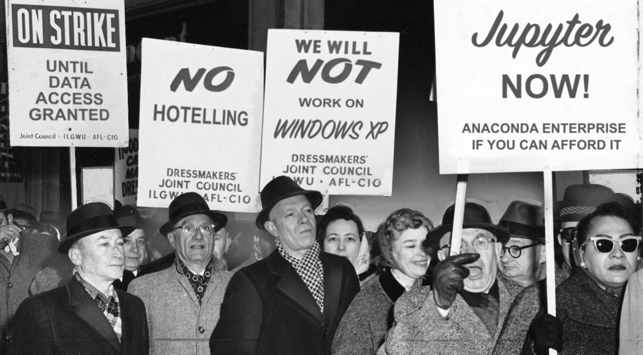 A black and white photo of people striking. The signs say, Jupyter now and no hotelling.